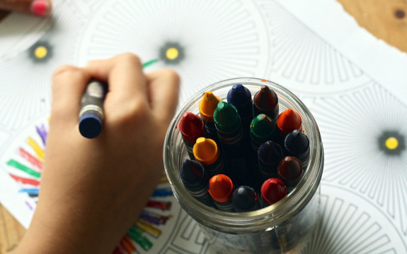 Kinderhand malt mit Buntstift, daneben steht ein Glas mit Wachsmalstiften: Quelle Pixabay